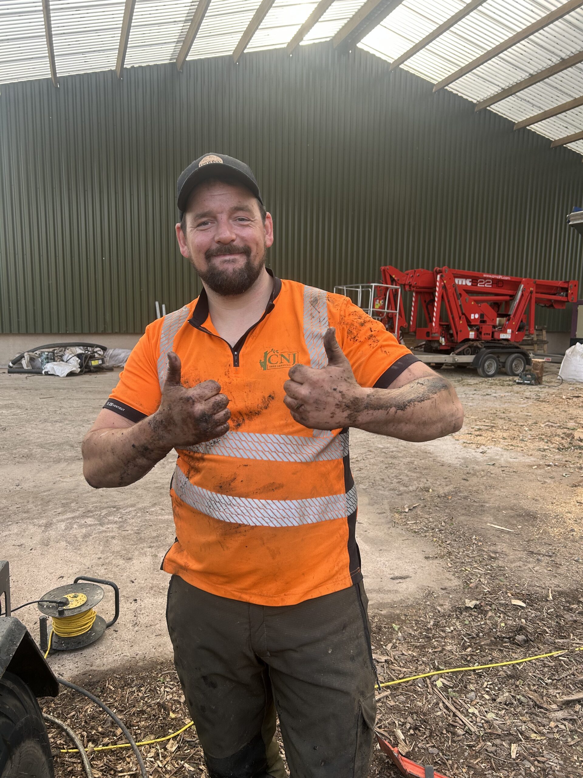 A muddy tree surgeon giving a thumbs up in the workshop.