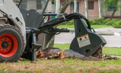 A skid-steer loader with a stump grinder attachment removing a tree stump on a grassy area.