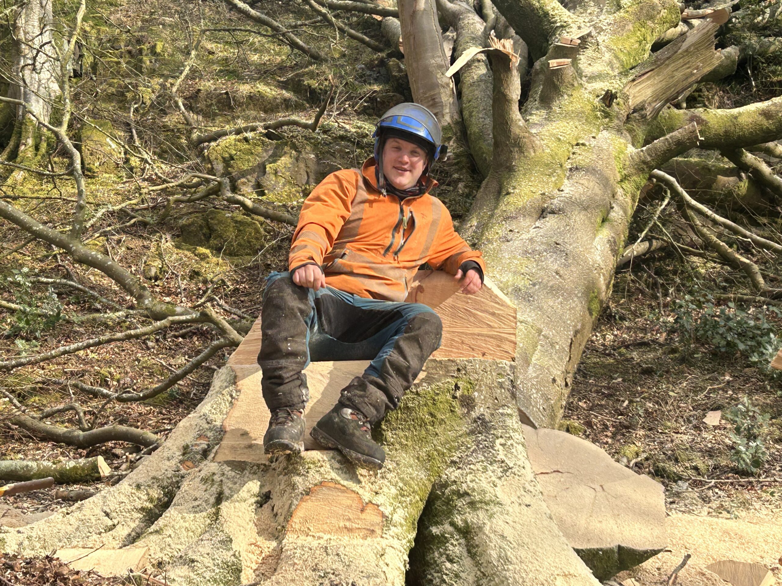 worker sitting smiling on large felled tree section